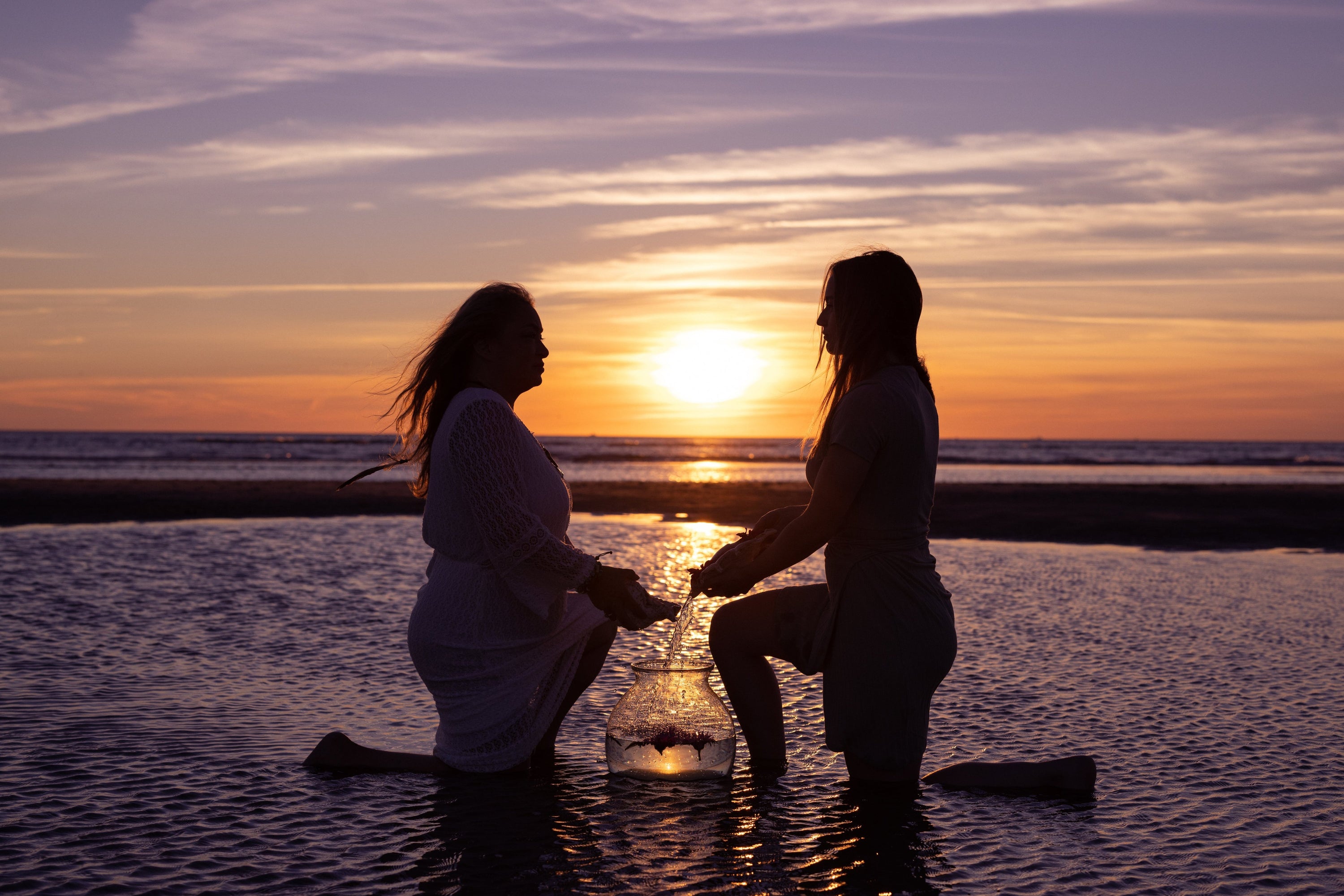 two woman on the beach at the sea pouring water in a bowl